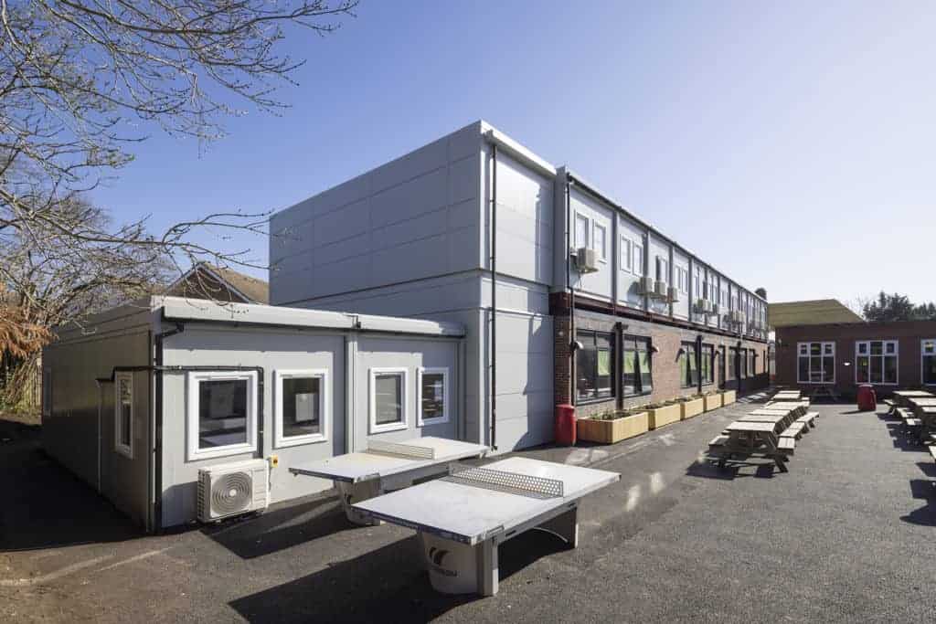 outside view of two-storey modular classrooms. Table tennis tables, as well as benches and tables filled the playground. 