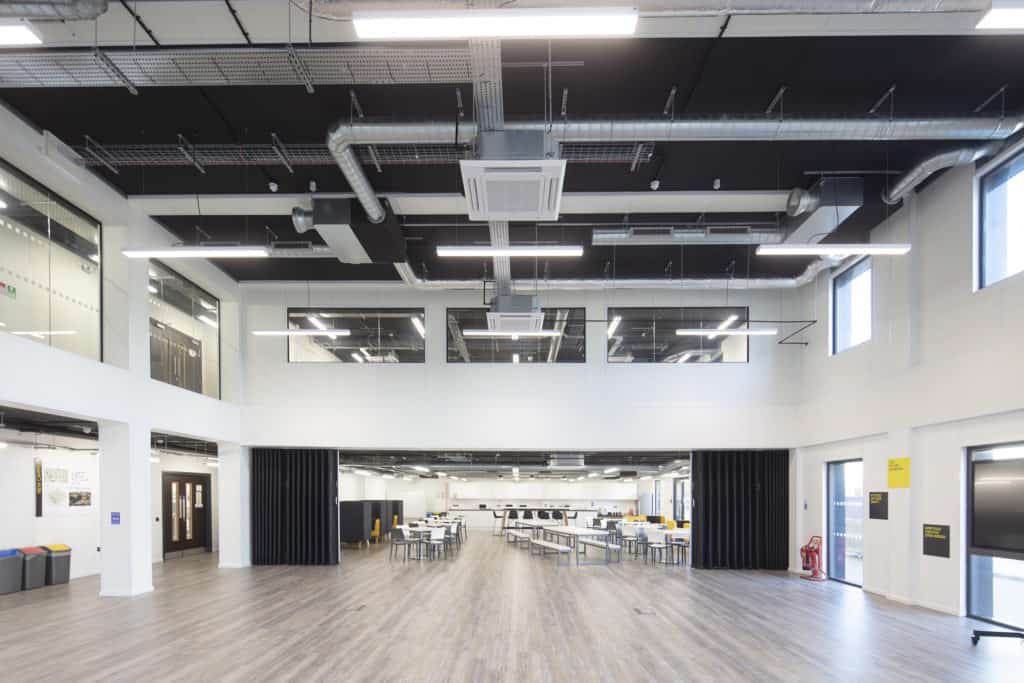 Inside view of modular classroom/ teaching space created for TEDI-London. Large spacious hall, with wall built to open and close with access to a classroom with desks and chairs. 