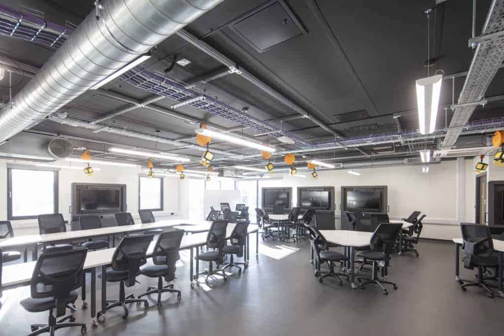 Inside a modular classroom, with desks and chairs in the area, and screens on the wall.