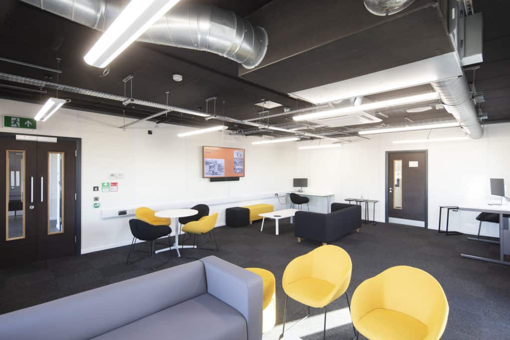 A lounge with yellow and black seating and sofas inside a temporary classroom facility.