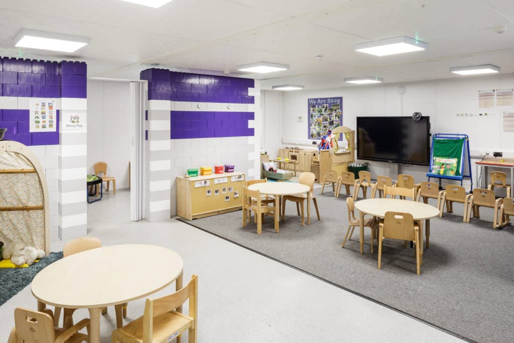 Inside the temporary classrooms, small wooden tables and chairs, large screen. Book cabinets. 