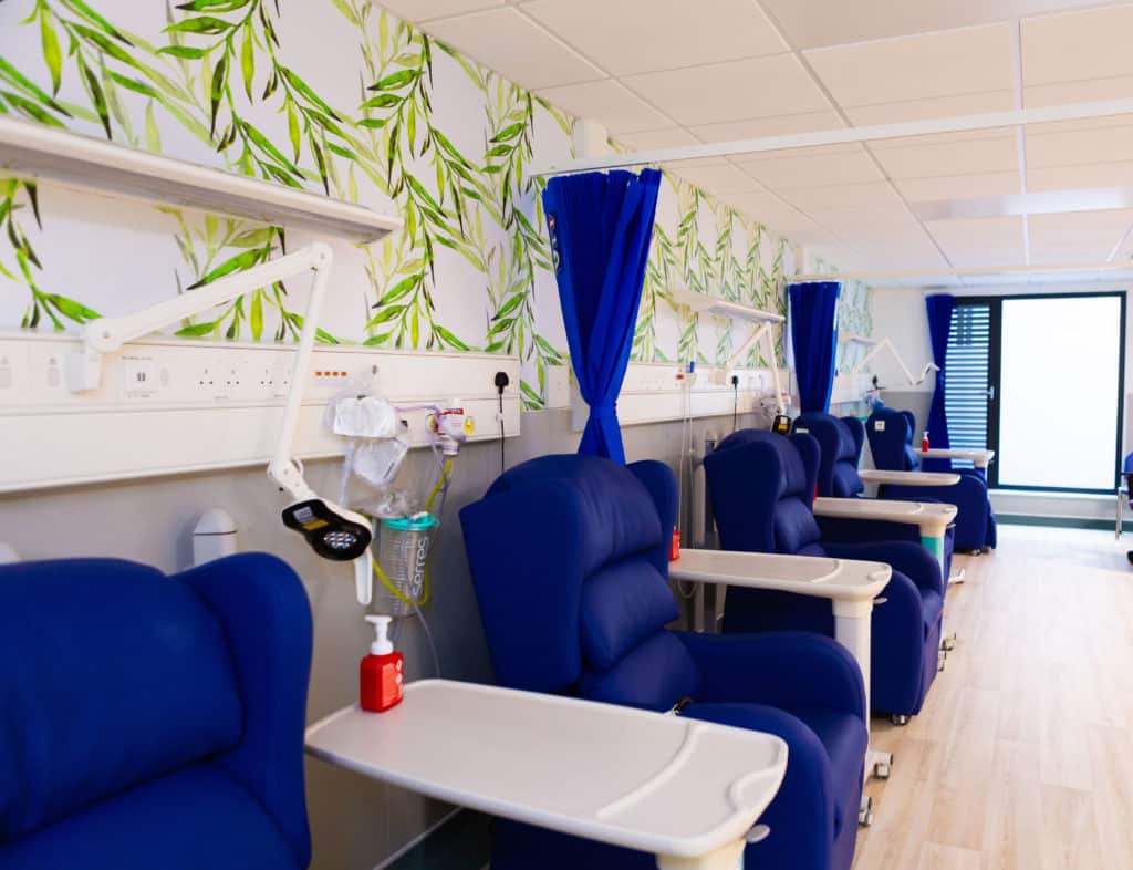 Infusion room in a hospital building built through offsite construction. Blue arm chairs with lap trays and medical equipment. 