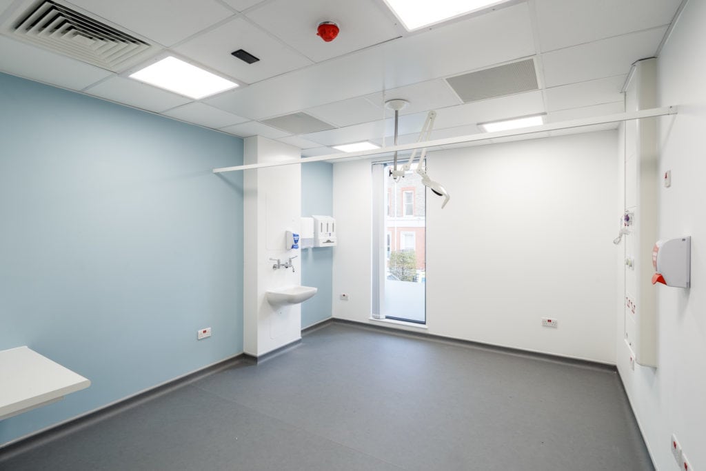 Hospital room inside a modular hospital building. Almost empty, with a sink attached to the wall and a soap dispenser. 