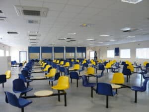 Onsite secure catering facilities for a prison, built offsite. Blue and yellow plastic chairs surrounding small circle tables. 