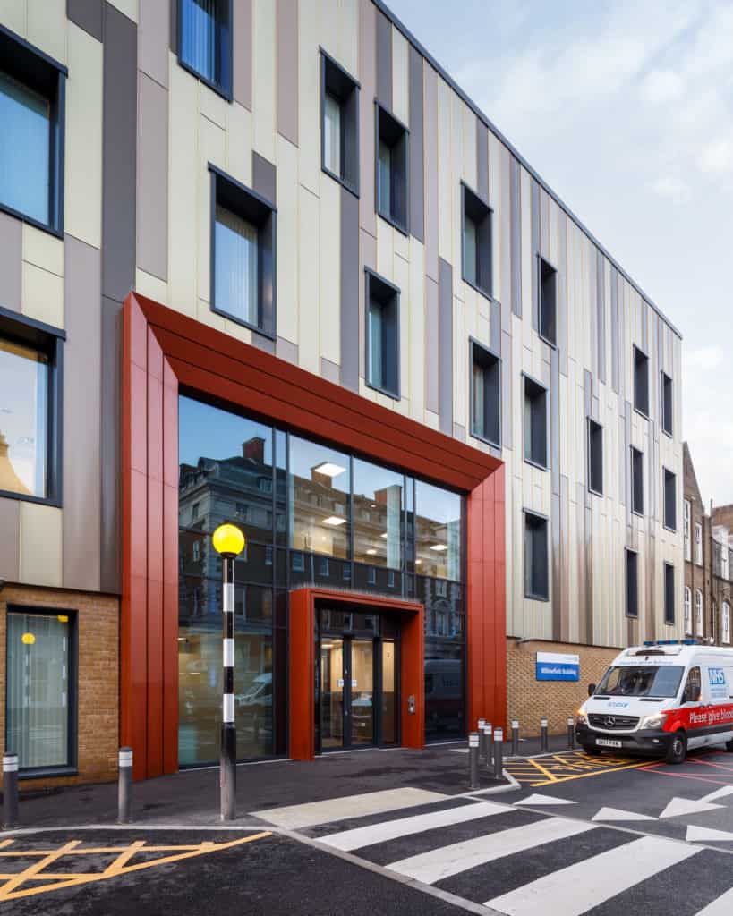 Modular Building for Kings College Hospital. View of the front of the modular hospital, entrance with glass doors, zebra crossing outside. Ambulance parked up. 