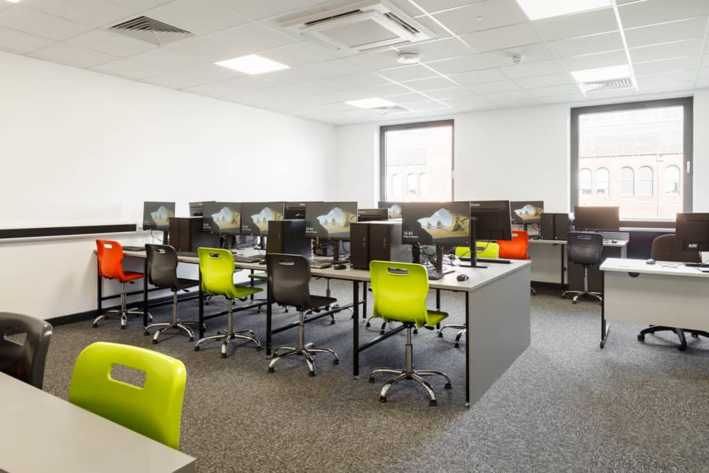 Inside a modular classroom filled with PC's and computer chairs. Chairs are a mix of orange, green and black. Grey carpet.