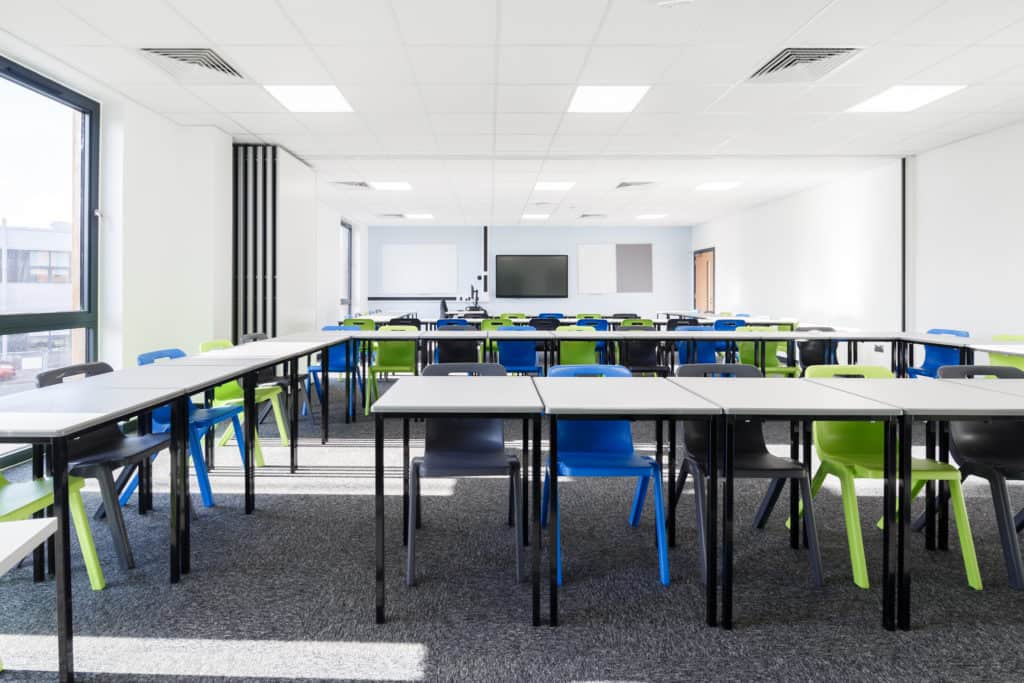 Two modular classrooms joined into one by sliding shut the middle wall. Several desk and chairs fill the room as well as a whiteboard and screen.