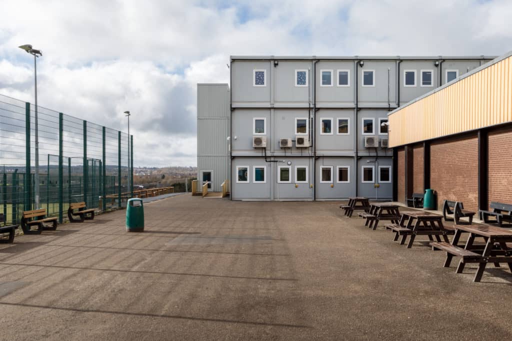 Outside view of the temporary classrooms and education buildings. Benches in the playground.