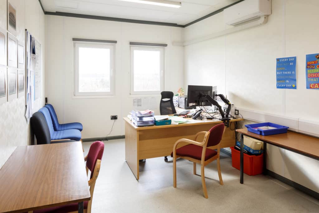 Office inside the modular classroom facility. Desk with a computer on, and some chairs for people to sit on whilst waiting. 