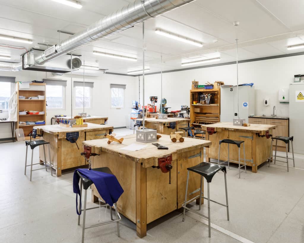 Inside a modular classroom. Desks and stools fill the room. 