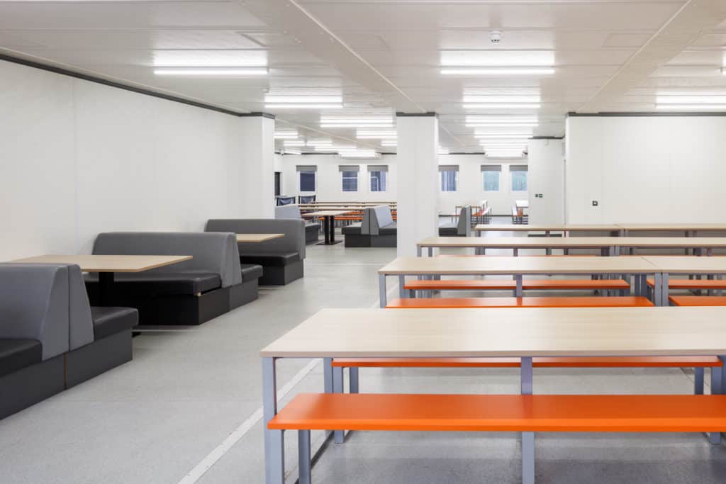 Seating area for lunch inside the modular school. Tables and benches where students will visit after lessons in the temporary classrooms.