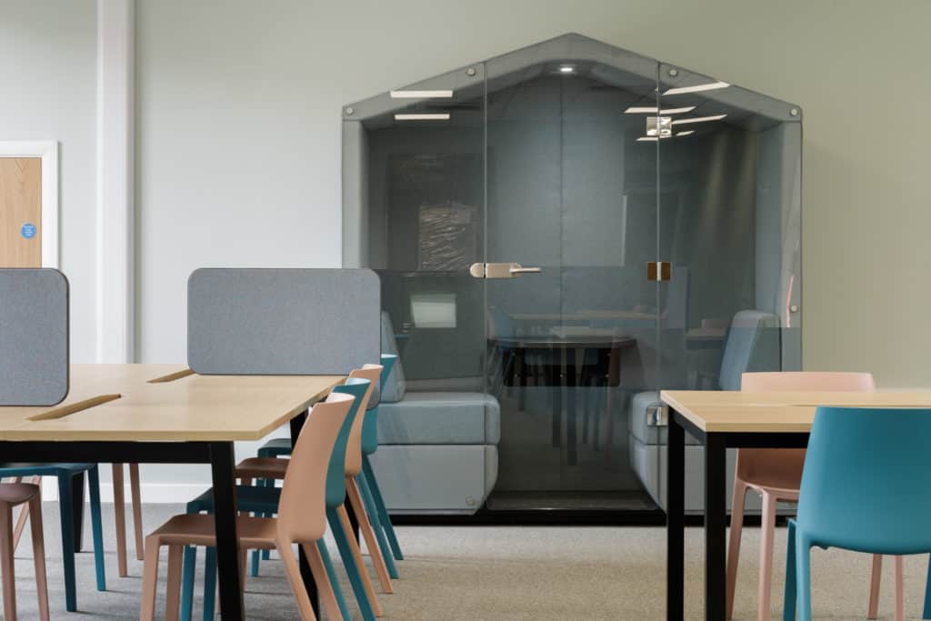 Inside a modular classroom. Study area with desks and chairs, and a hut for enclosed learning. 