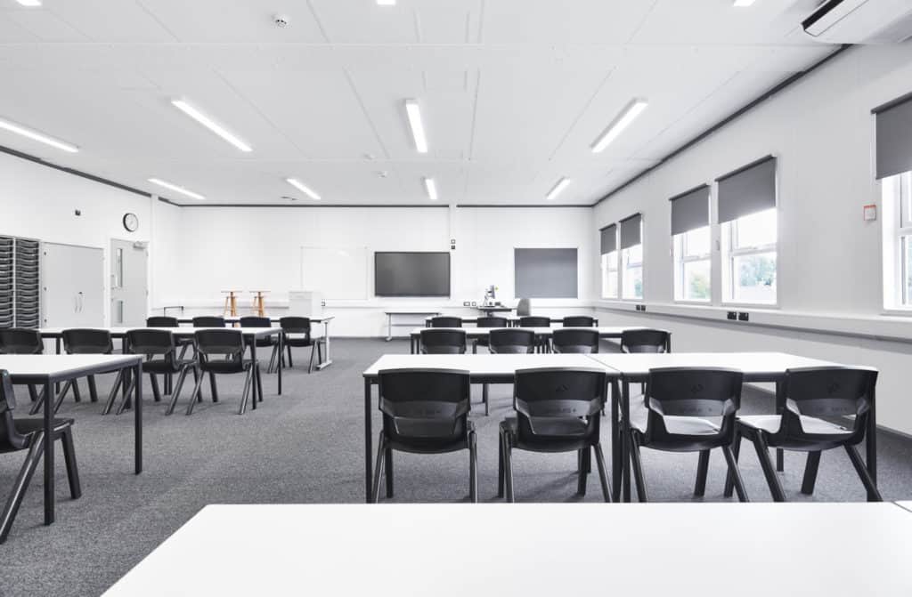 Inside modular classroom. Several tables and chairs in front of an interactive whiteboard, and teachers desk at the front of the room.