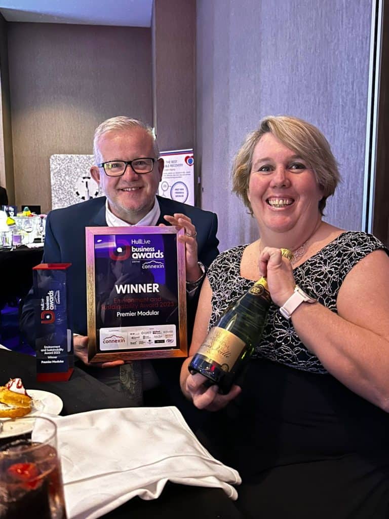 2 members of the team. One holding up the Environment and Sustainability Award, and the other holding a bottle of champagne. 