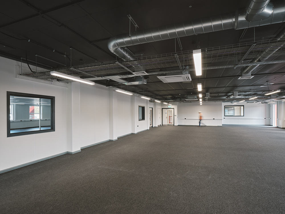 Large empty room inside temporary modular building. White walls. Grey carpet. 