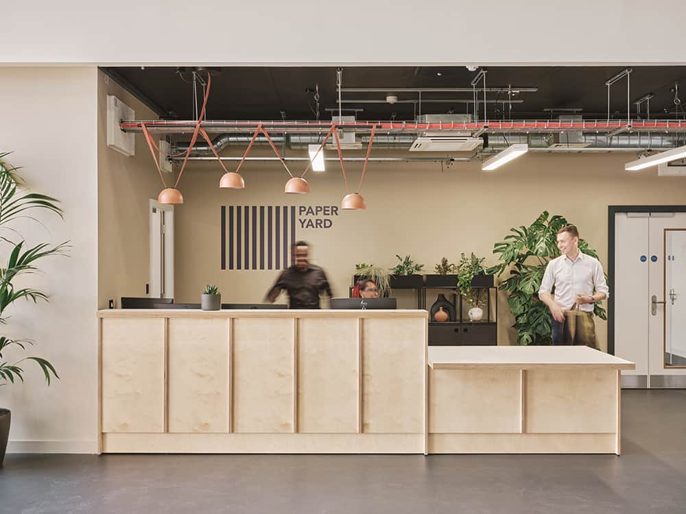 Reception area inside temporary modular building The Paper Yard. Welcome desk, with two employees. 