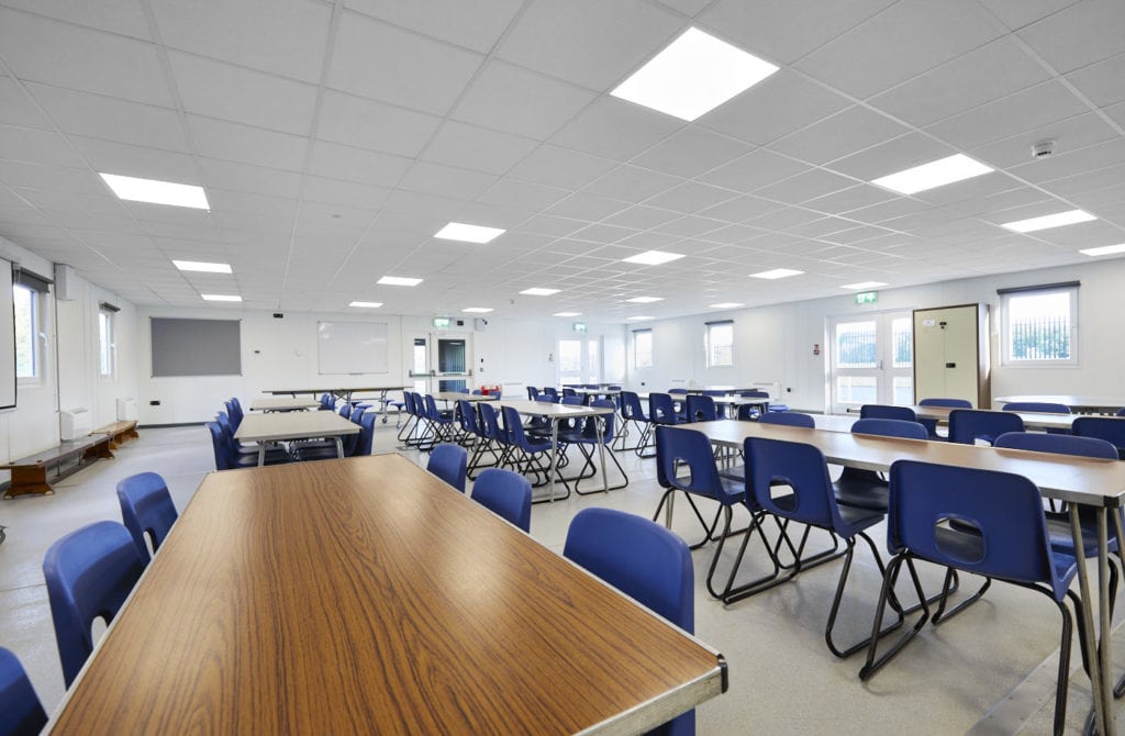Inside a room in the Modular school building. Rectangular tables surrounded by chairs. 