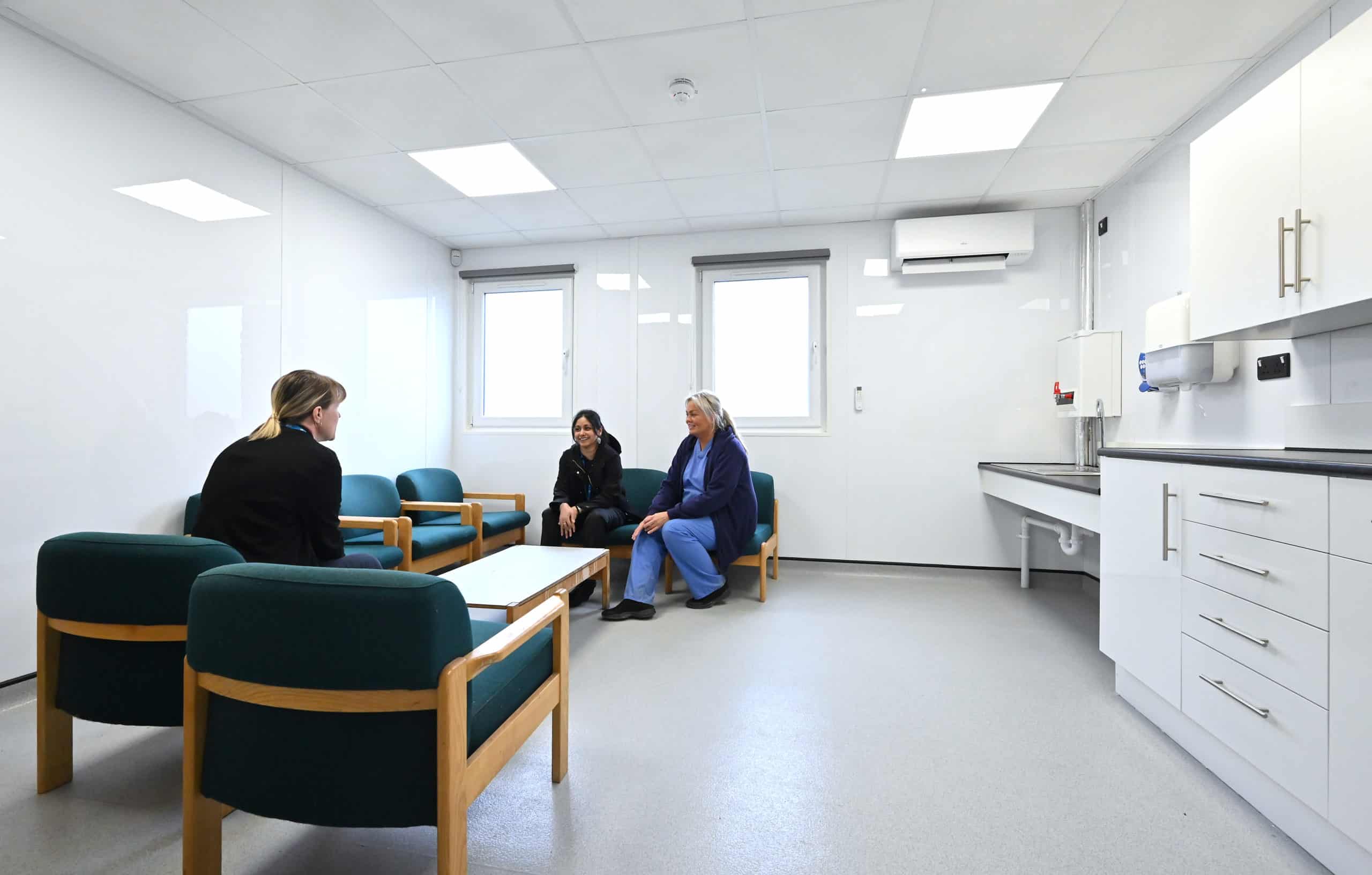 Staff waiting area inside modular hospital. Chairs with a coffee table and a sink and cabinets. 