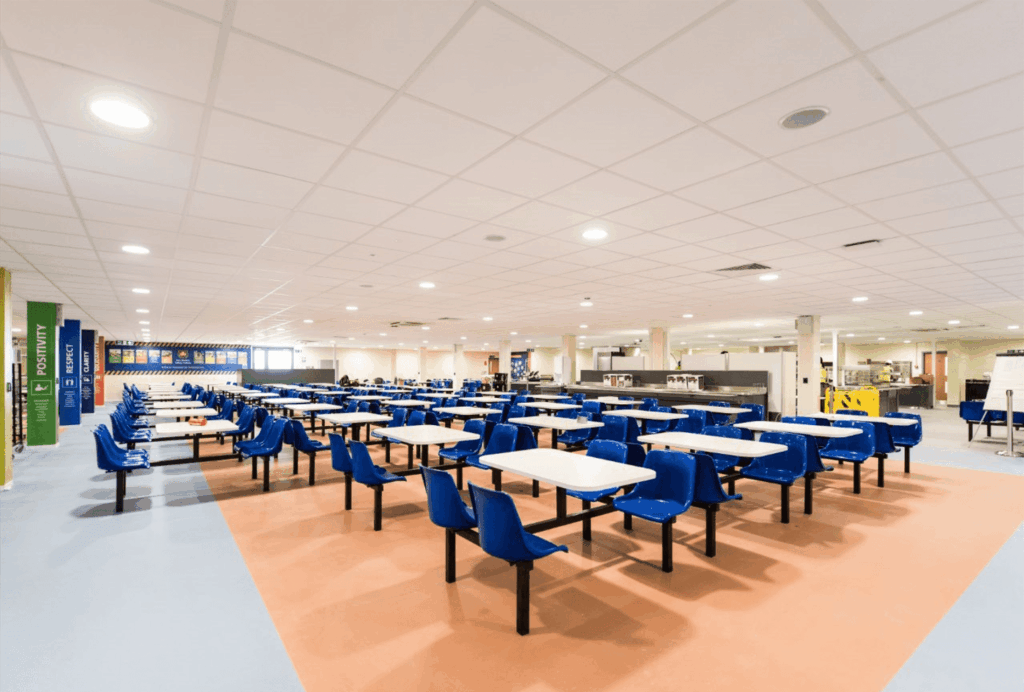 Cafeteria. Lots of tables with plastic chairs, inside a modular building. 