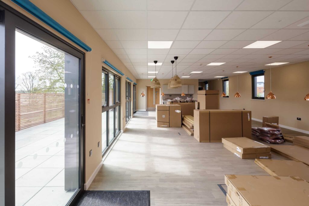 Inside a modular building, in the process of being finished. Glass windows, bright walls, lots of natural lighting. cardboard boxes spread over the floor.