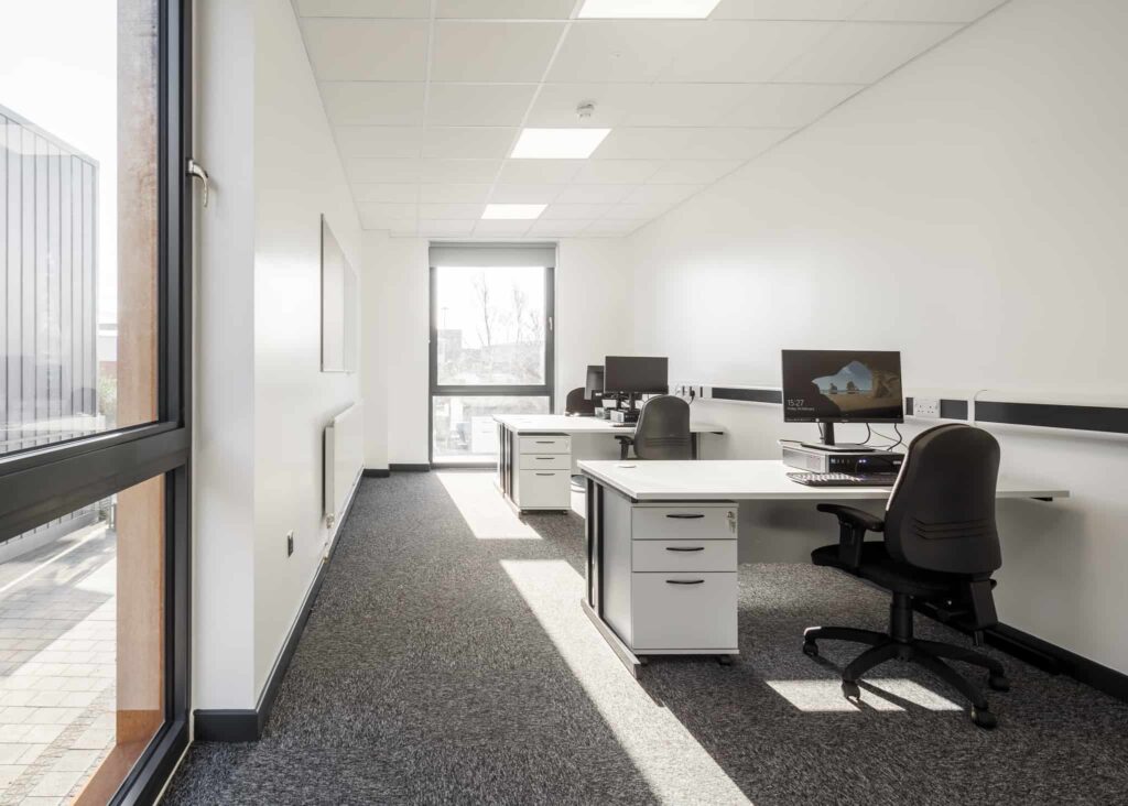 White walled room inside the modular buildings built for Leeds City Council. 2 desks with computers and chairs, both with 3 drawers.
