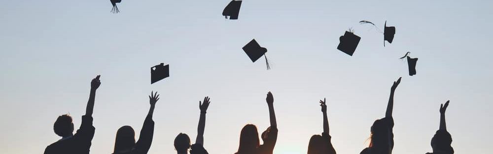 Sillhouette of students throwing their graducation caps into the air. 